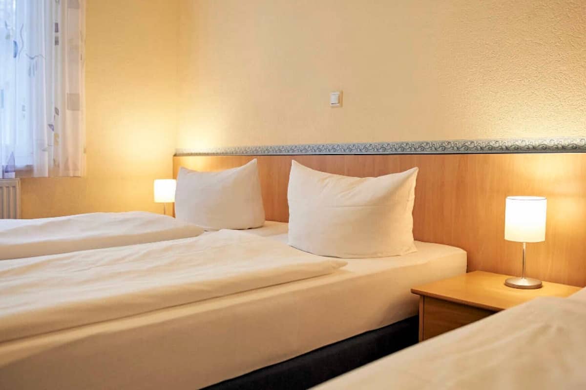 Een hotelkamer met twee bedden, elk voorzien van witte lakens en kussens, een houten hoofdeinde en een bedlampje.