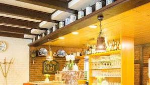 Zona de bar con taburetes de madera, pared de ladrillo y estanterías con botellas y vasos.