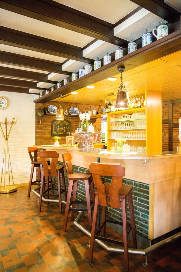 Un espace bar avec des tabourets en bois, un mur en briques et des étagères remplies de bouteilles et de verres.