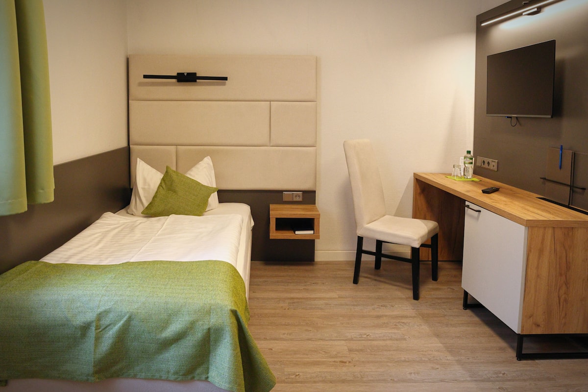 Una habitación de hotel con cama, escritorio, silla, televisión y mesita de noche.