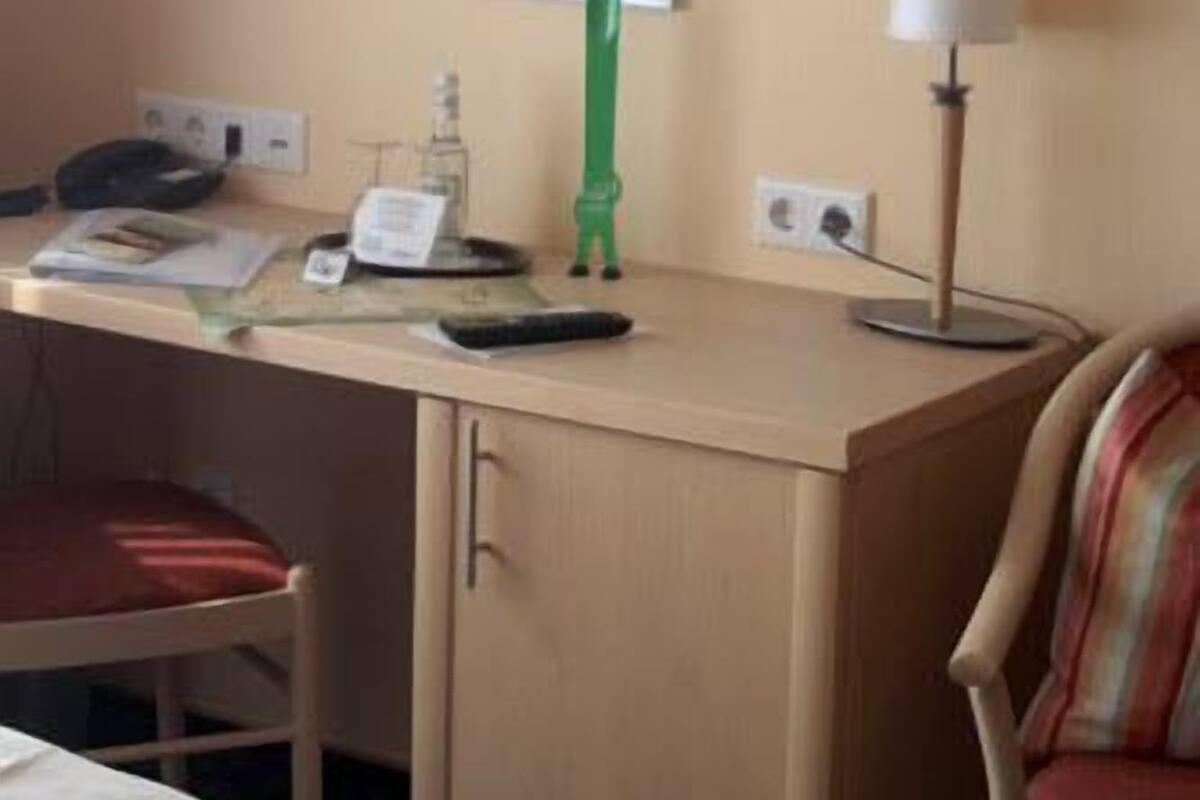 A hotel room with a desk, a television mounted on the wall, a lamp, and a chair.