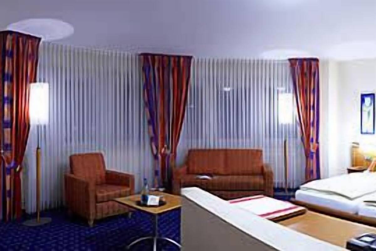 A hotel room with a bed, a desk, two chairs, a small table, and a window with curtains.