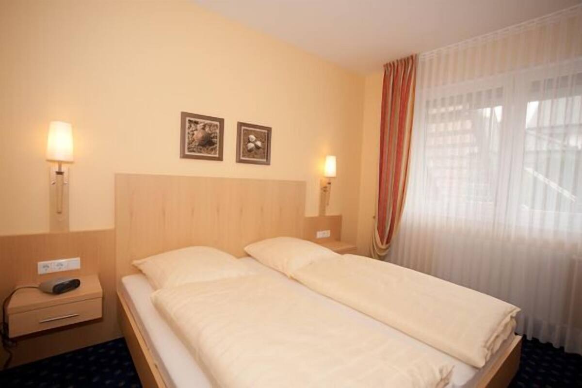 A hotel room with a double bed, two bedside tables, a lamp, and a window with curtains.
