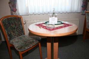 A round table with a placemat, a glass, and a bottle of water. There is a chair with a patterned cushion next to the table. - Akzent Hotel Hubertus (Melle)