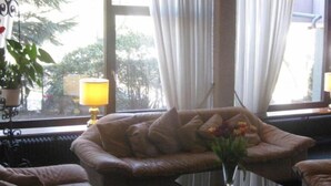 A room with a leather sofa, a small table with a lamp, and a window with curtains. - Hotel am Klostersee (Sindelfingen)