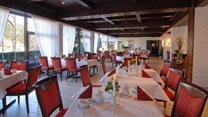 A restaurant with tables set for dining, red upholstered chairs, and a view of the outdoors through large windows. - Hotel am Klostersee (Sindelfingen)