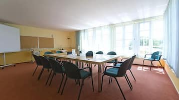 Un salón de conferencias con una larga mesa, sillas, una pizarra y ventanas amplias.