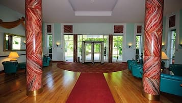 A spacious lobby with a red carpet, marble pillars, and teal sofas.