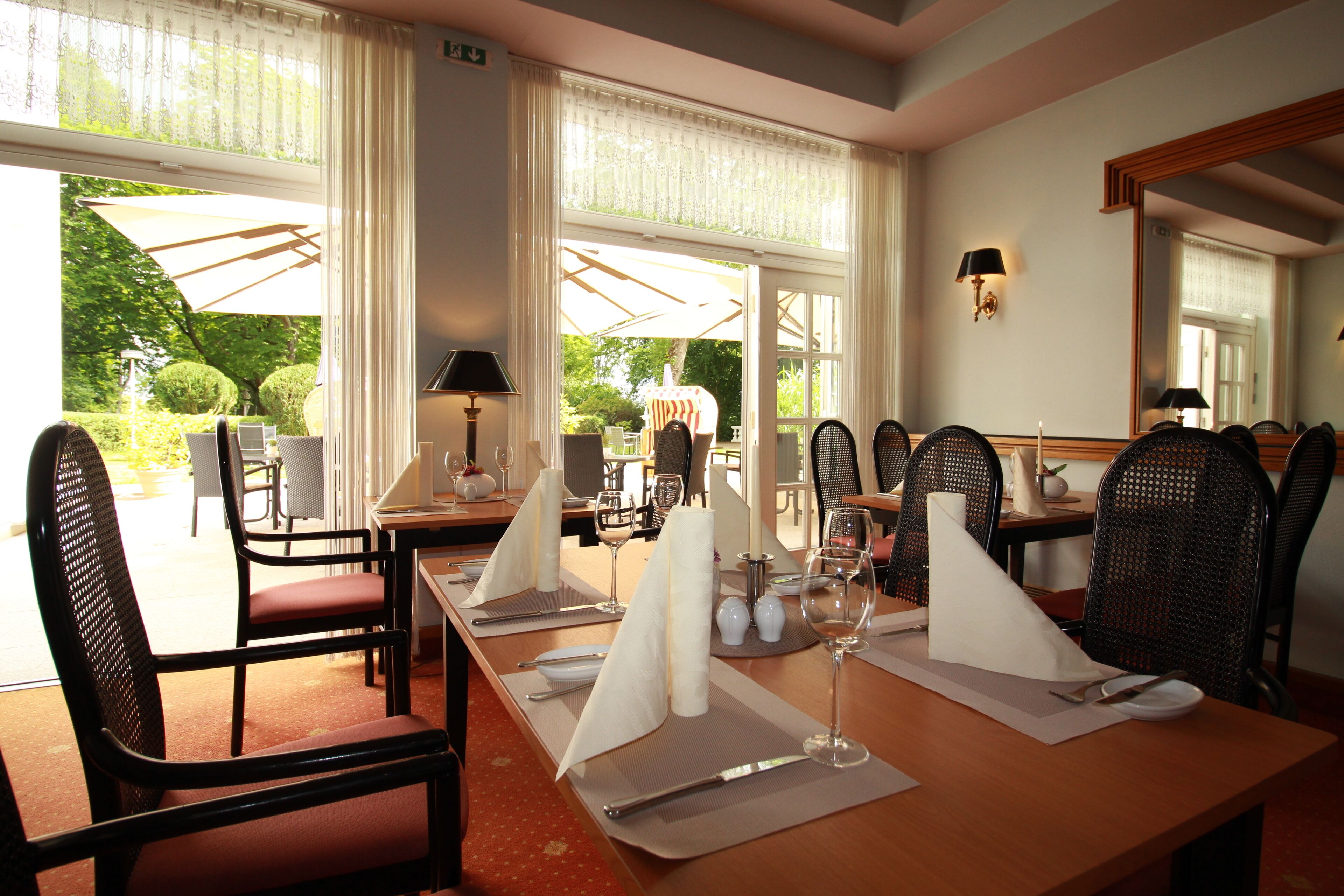 A dining area with a long table set for a meal, surrounded by chairs, and large windows with curtains.