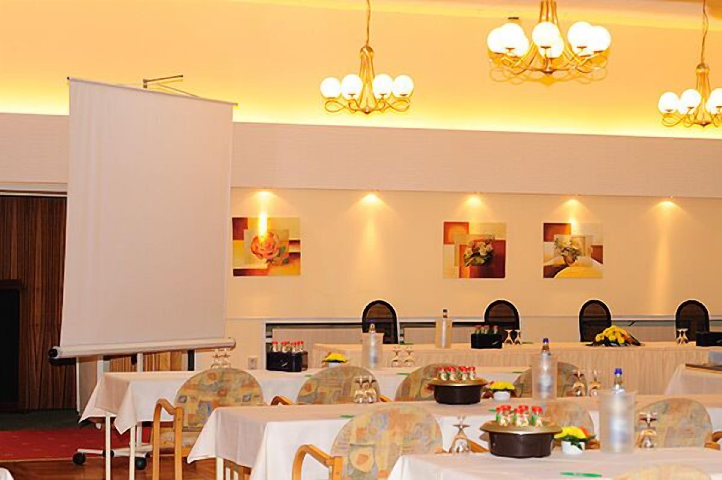 Un salón de banquetes con mesas dispuestas para una comida, una pantalla de proyector y obras de arte colgadas en la pared.