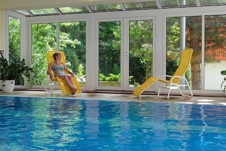 Una piscina techada, sombrillas, sillones reclinables de piscina. Parkhotel Klüschenberg