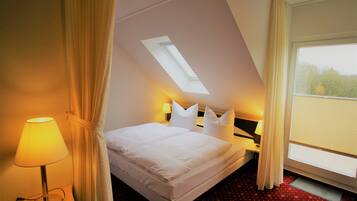 Ein Hotelzimmer mit einem Bett, einem Nachttisch, einer Lampe, einem Fenster mit Vorhängen und einem Oberlicht.