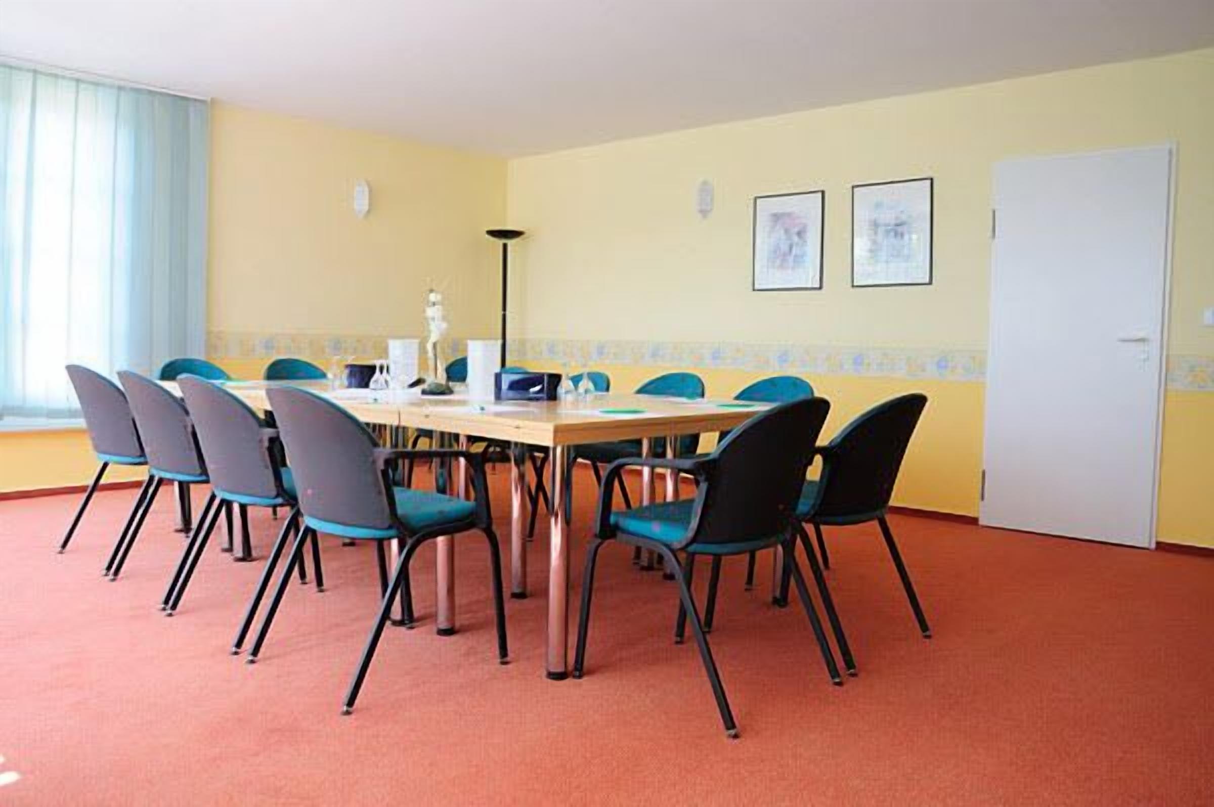Une salle de conférence avec une longue table et huit chaises, une porte blanche et deux tableaux encadrés au mur.