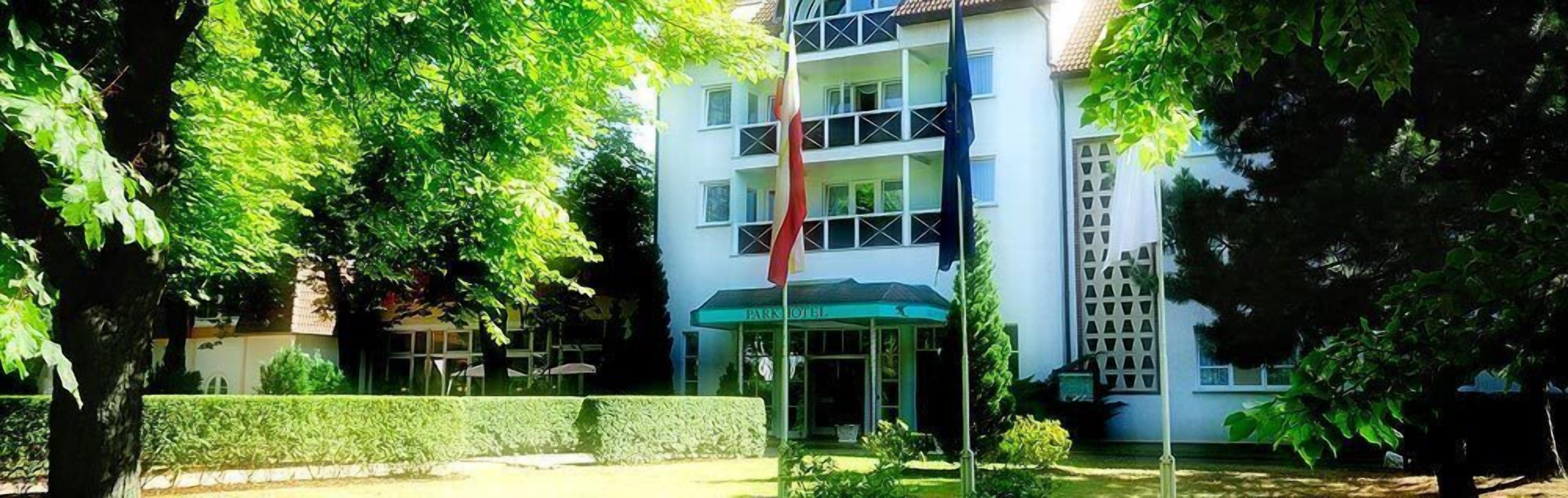 A hotel with a central entrance, surrounded by lush greenery and a well-maintained hedge.