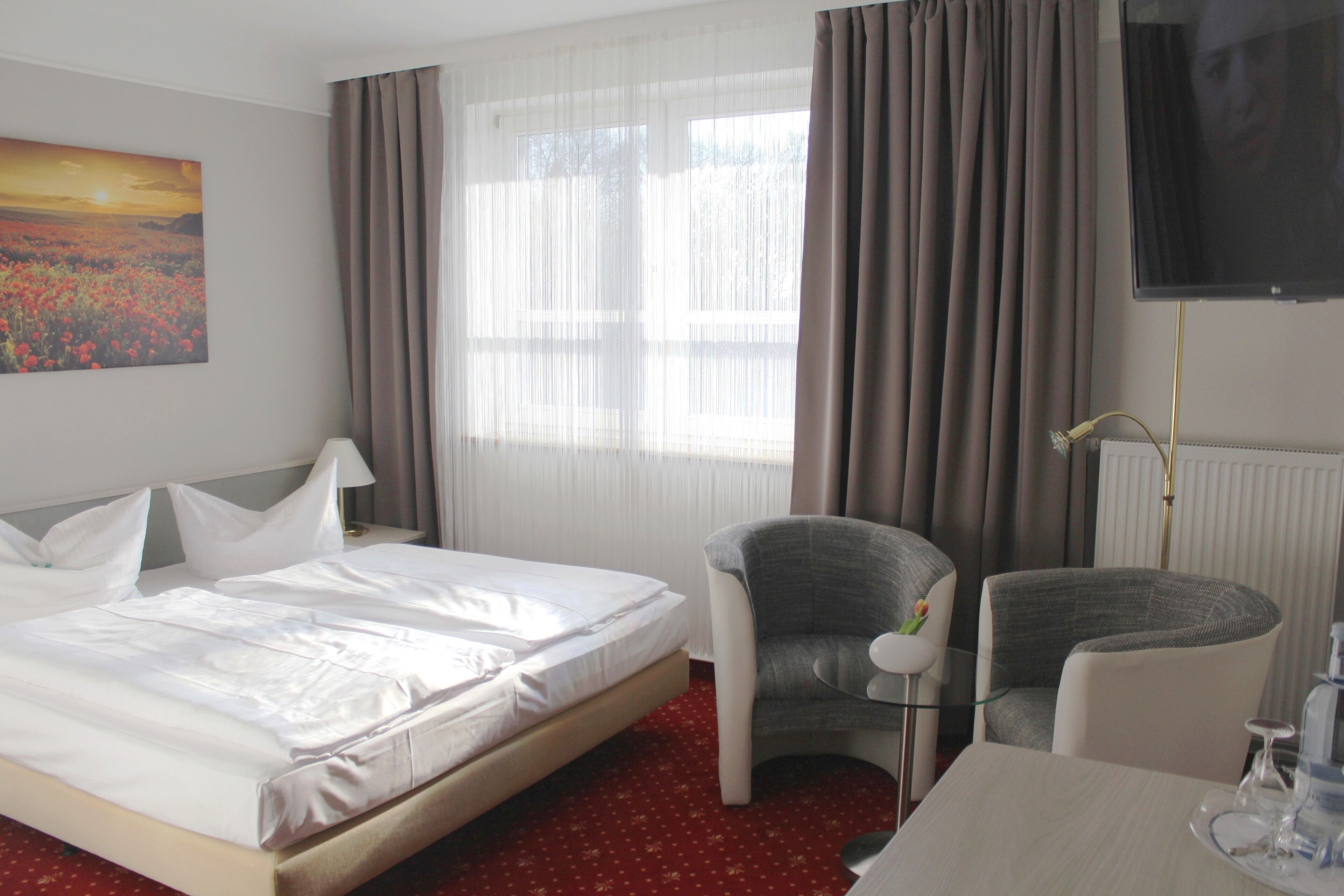 A hotel room with a bed, two armchairs, a table with a tray, a TV, and a painting on the wall.
