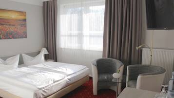 A hotel room with a bed, two armchairs, a table with a tray, a TV, and a painting on the wall.