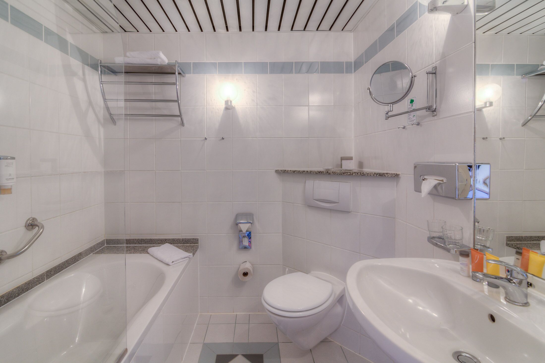 A modern bathroom with a bathtub, toilet, and sink, equipped with a towel rack, hand dryer, and a mirror.