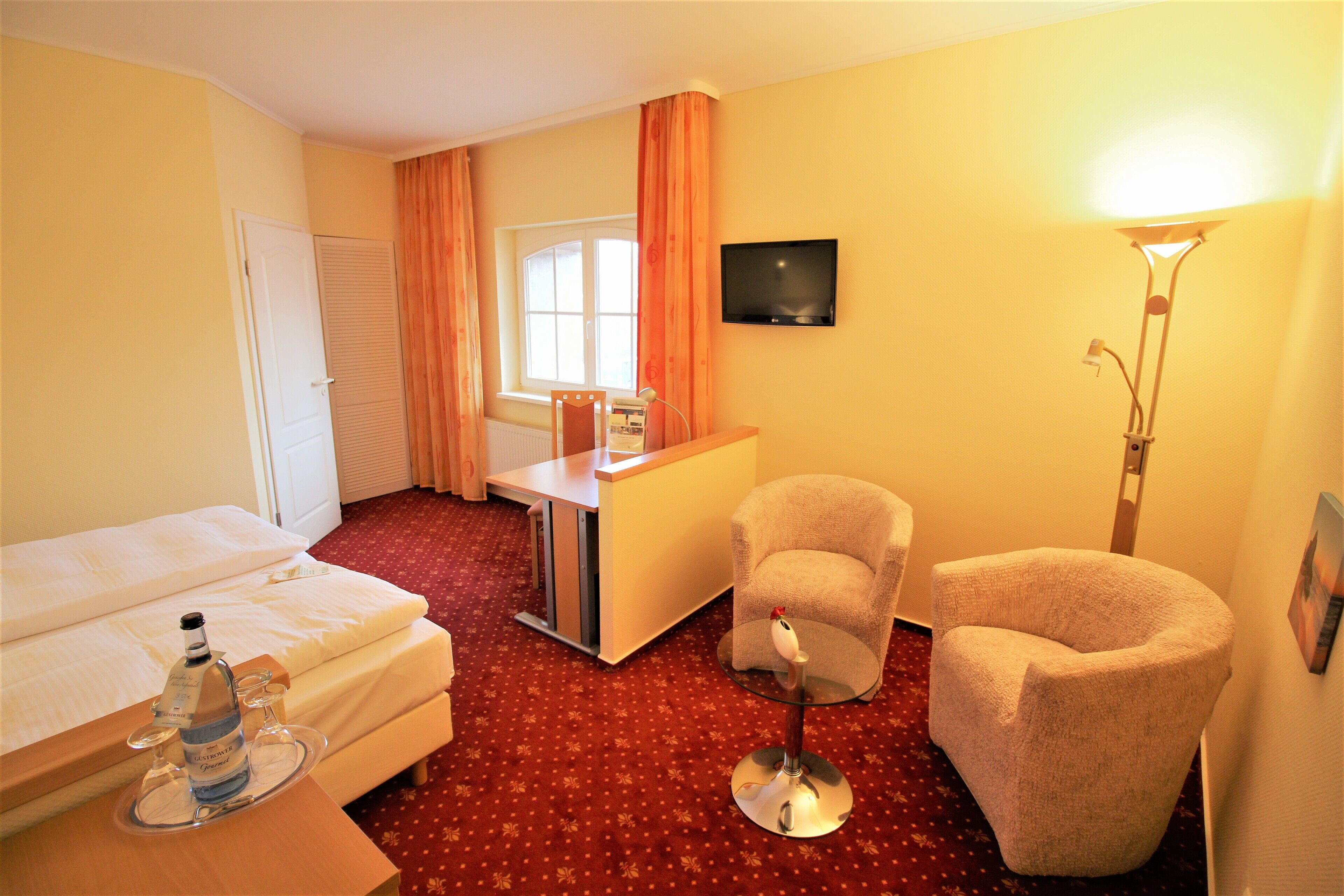 Ein Hotelzimmer mit einem Bett, einem Schreibtisch, zwei Sesseln, einem Fernseher und einer Lampe.