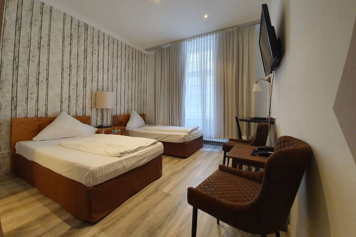 A hotel room with two beds, a desk, a chair, a TV, and a window with curtains.
