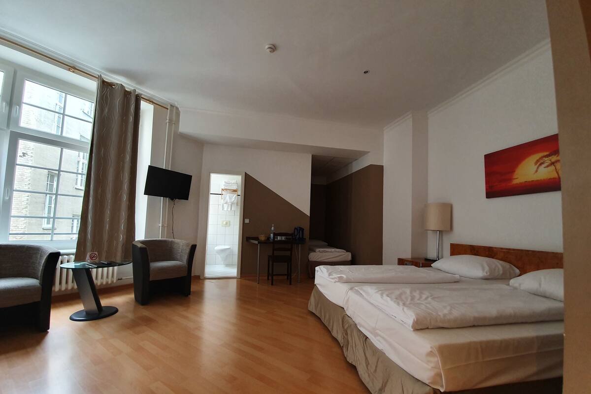 A hotel room with a bed, a desk, a chair, a TV, and a window with curtains.