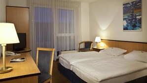 A hotel room with a bed, a desk with a lamp, a chair, a television, and a painting on the wall.