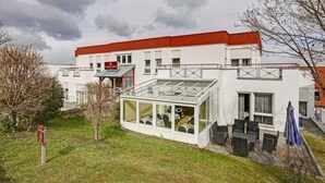 A hotel with a red roof, a covered outdoor seating area, and a sign indicating a parking area.