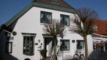 Ein weißes Haus mit zwei Etagen, einem grünen Dach, einer Haustür und einer kleinen Veranda mit einem Fahrrad.