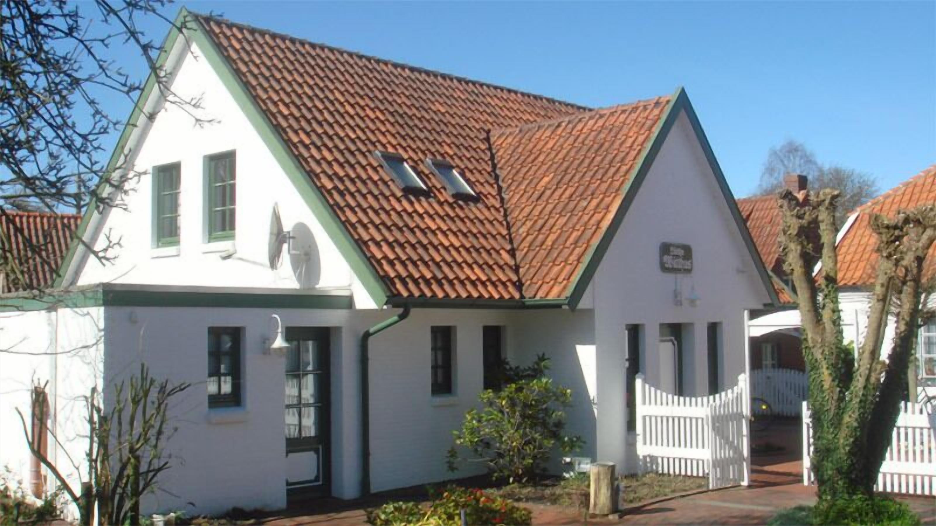 Ein zweigeschossiges Haus mit rotem Ziegeldach, weißen Wänden und einer kleinen Veranda.