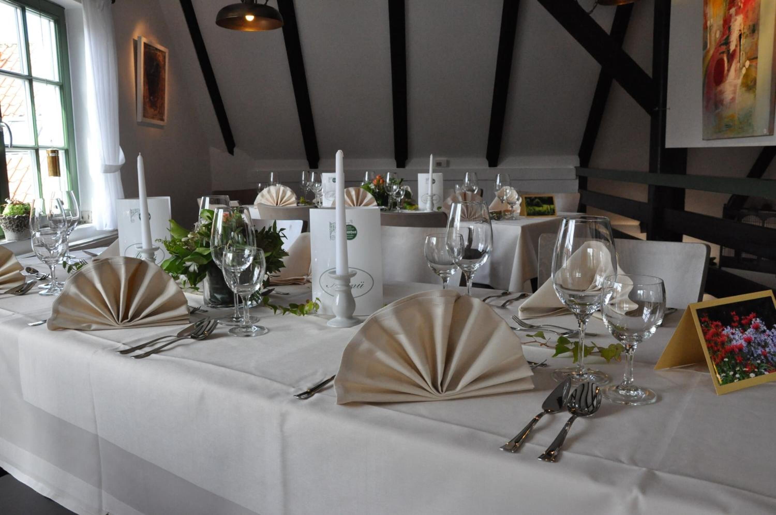 Una larga mesa de comedor vestida con manteles blancos, servilletas doradas y cristalería.