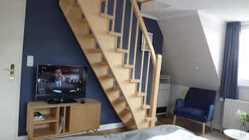 A bedroom with a wooden staircase, a television, a blue chair, and a bed.