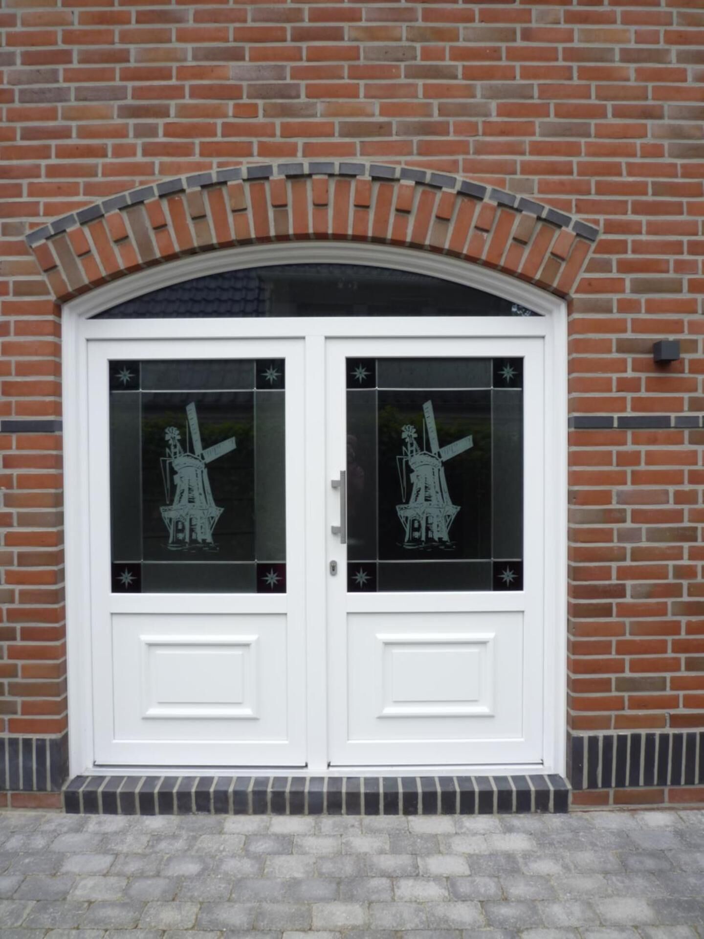 A double white door with glass panels, set in a brick wall.