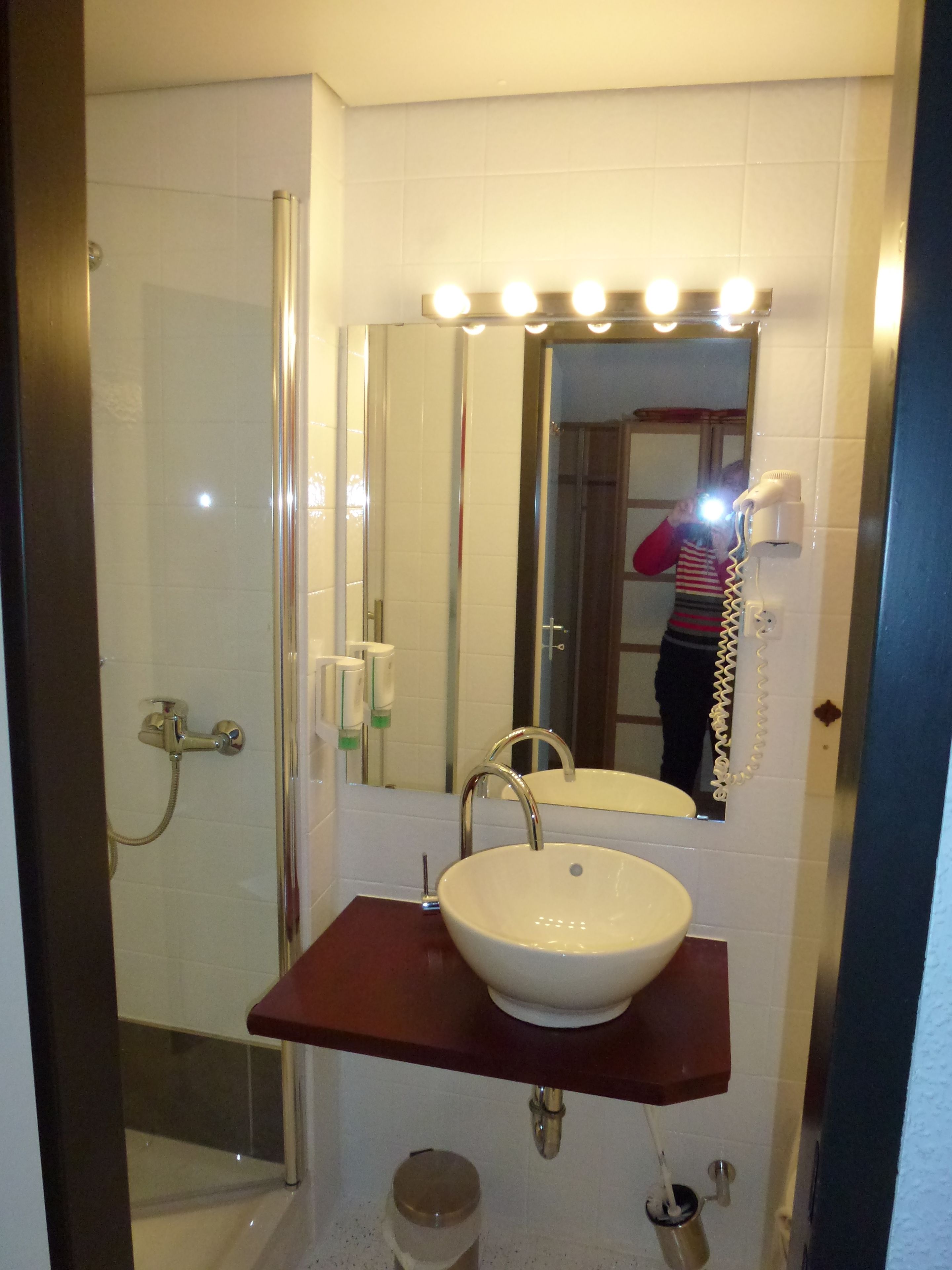 Une salle de bain avec un lavabo blanc, un miroir avec éclairage intégré, une douche et des toilettes.