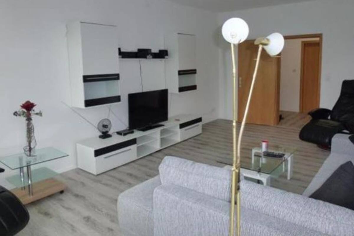 A modern living room with a grey sofa, a flat-screen TV, a glass coffee table, and a floor lamp.