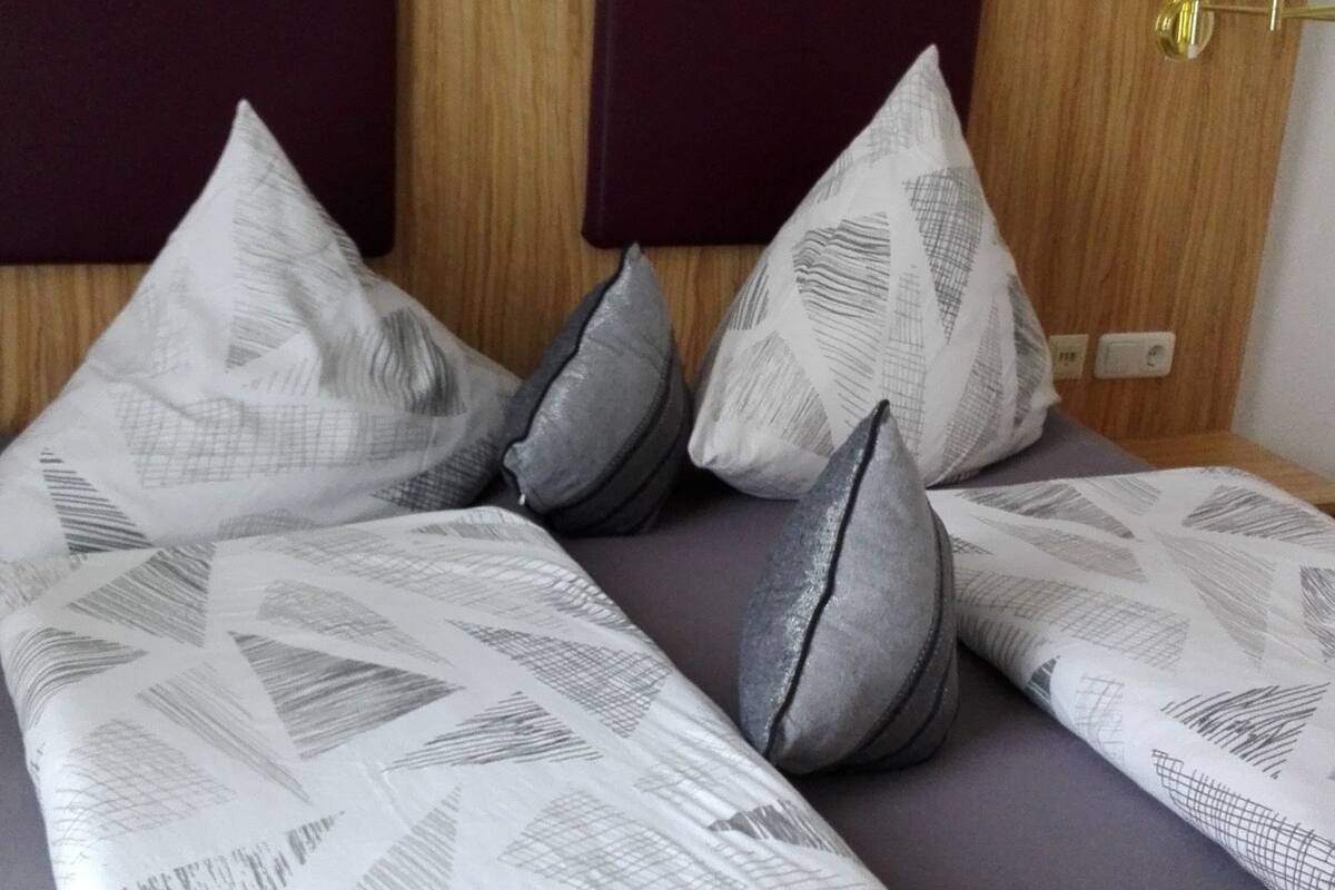 A bed with a patterned bedspread, multiple pillows, and a headboard with a light fixture.
