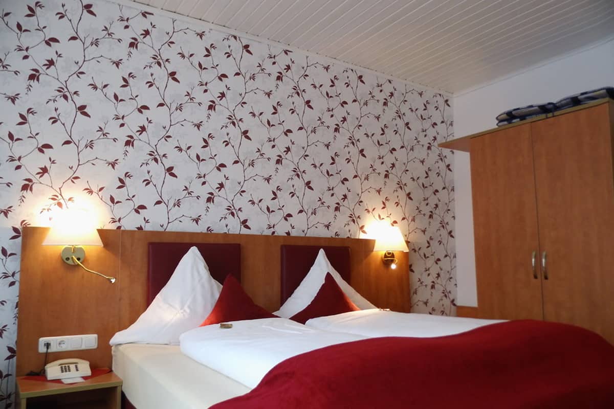 A hotel room with a bed, two bedside lamps, a nightstand, and a wardrobe.