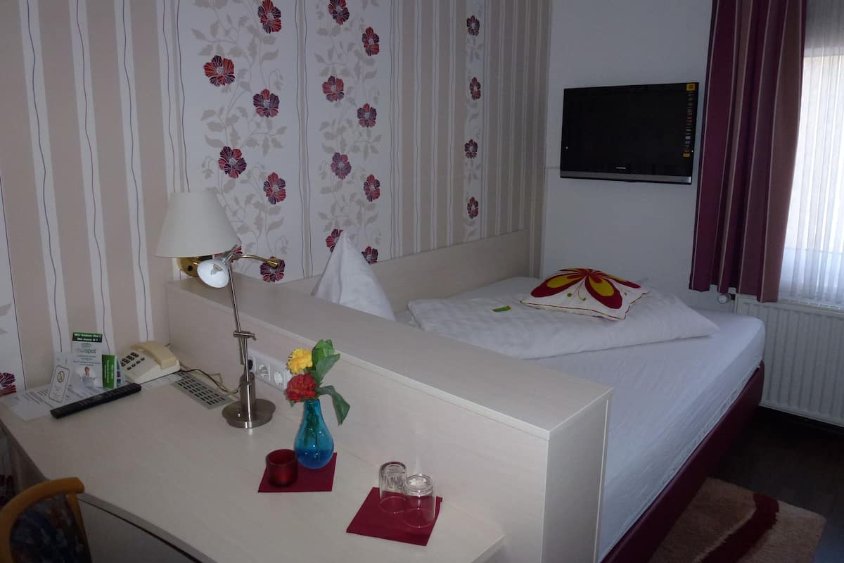 A hotel room with a bed, a desk with a lamp, a TV, and a window with curtains.