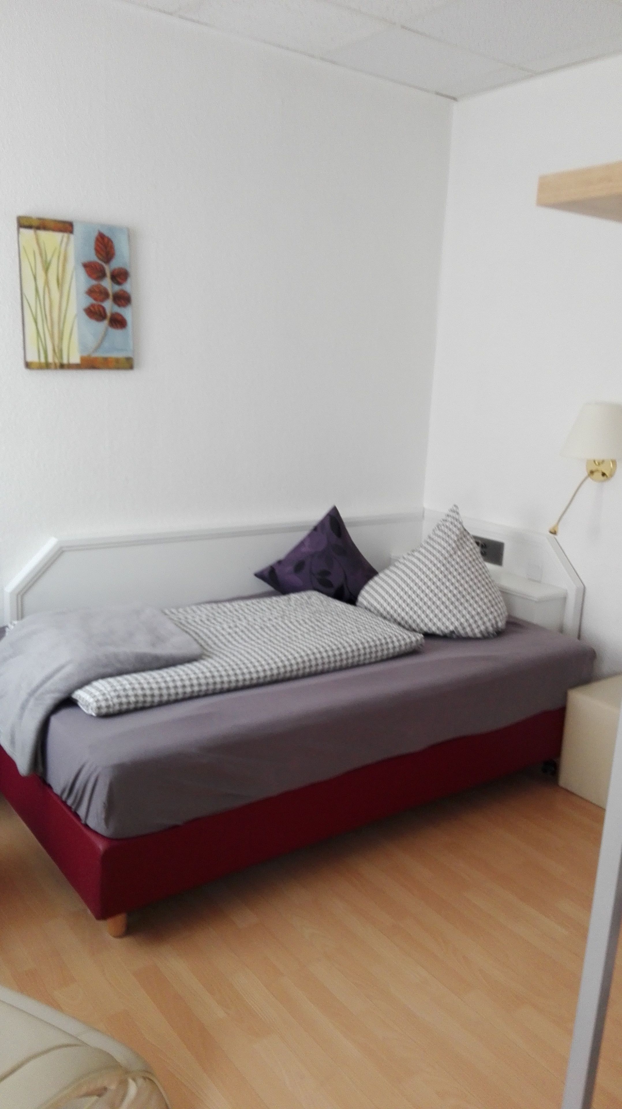 Ein Bett mit rotem Gestell, grauer Bettwäsche und mehreren Kissen.