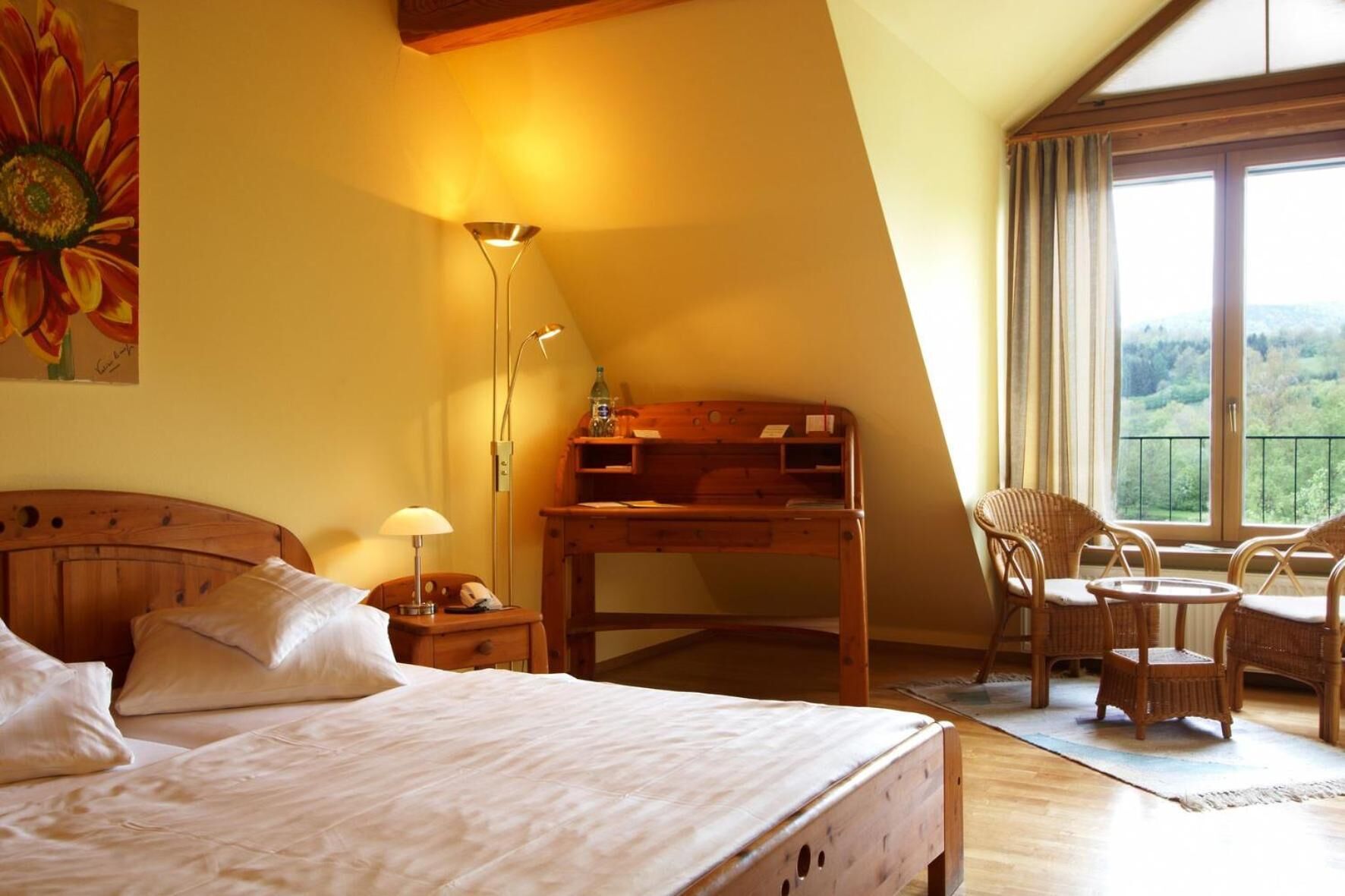 Quarto com cama, escrivaninha, cadeira e vista para uma paisagem verde através de uma janela.