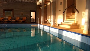 Una piscina interior con agua azul cristalina, cubierta de madera y sillones de descanso.