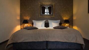 A large bed with a beige cover, two bedside lamps, and a mirror above it.
