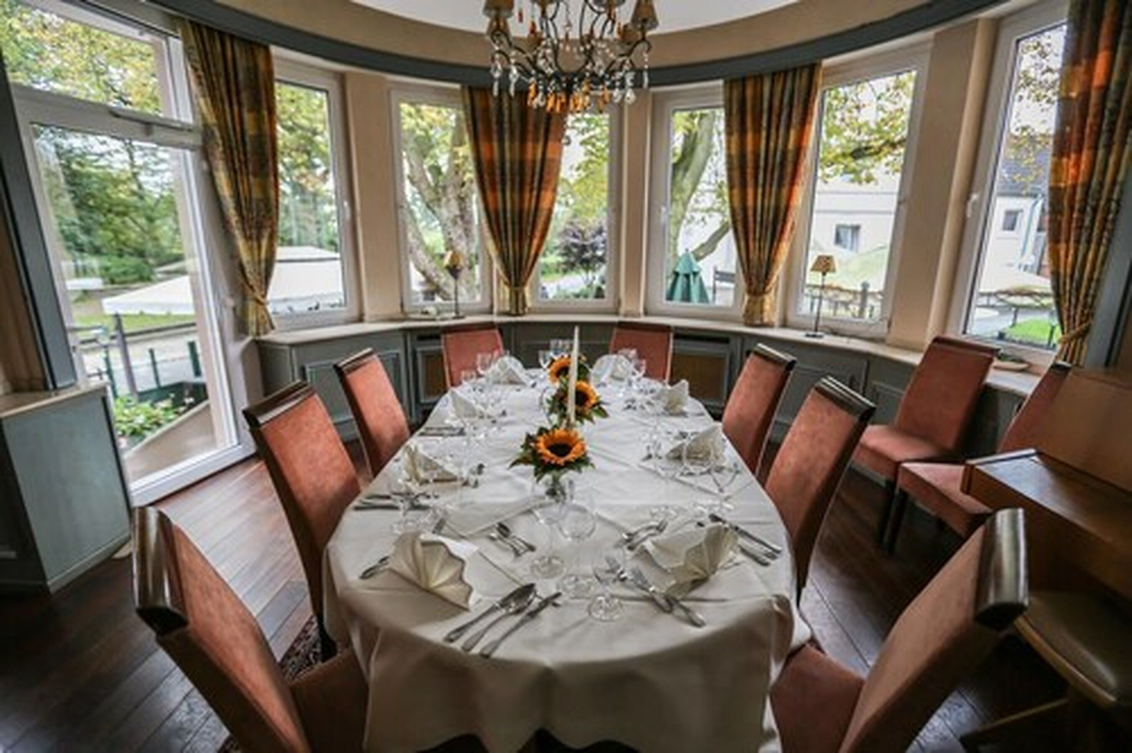 Ein Esszimmer mit rundem Tisch, gedeckt für sechs Personen, großen Fenstern und Blick ins Freie.