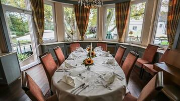 Ein Esszimmer mit rundem Tisch, gedeckt für sechs Personen, großen Fenstern und Blick ins Freie.