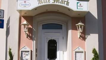 Ein Hotel Eingang mit einer weißen Tür, einem Schild mit der Aufschrift 'Hotel Restaurant Alte Falk' und je einem kleinen Blumentopf auf beiden Seiten.