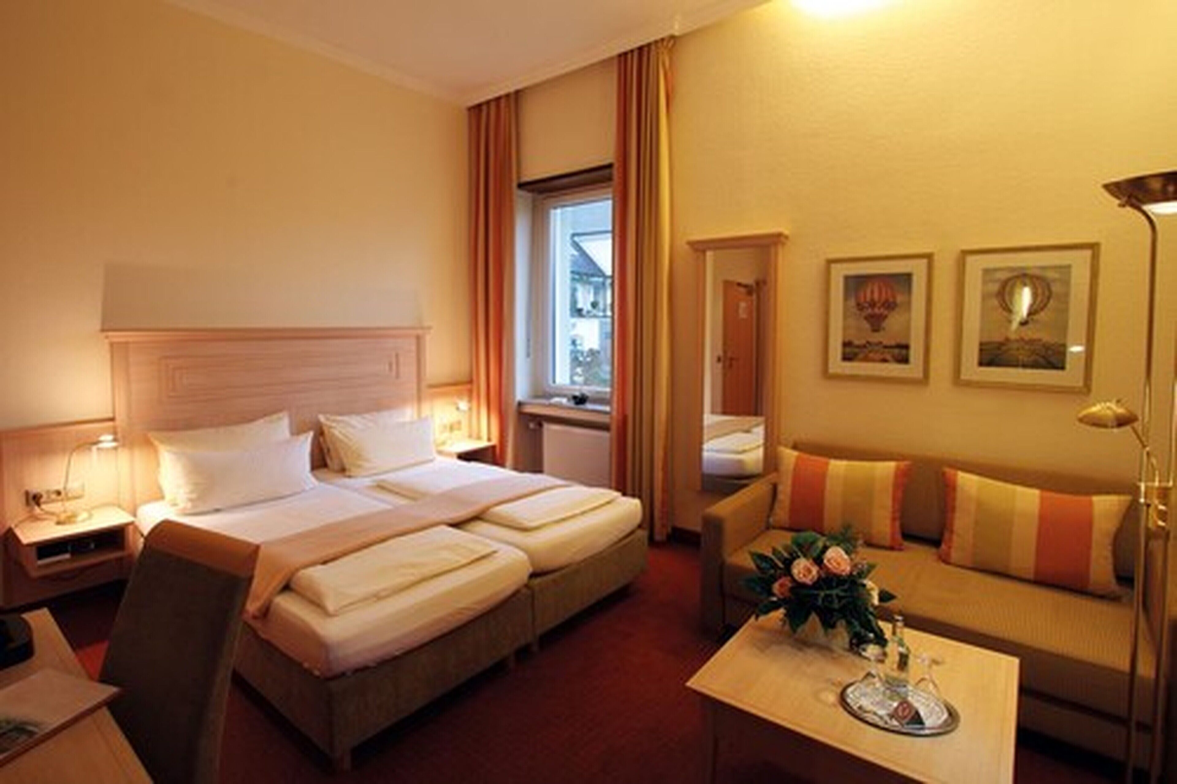 A hotel room with two beds, a sofa, a coffee table with flowers, and framed pictures on the wall.
