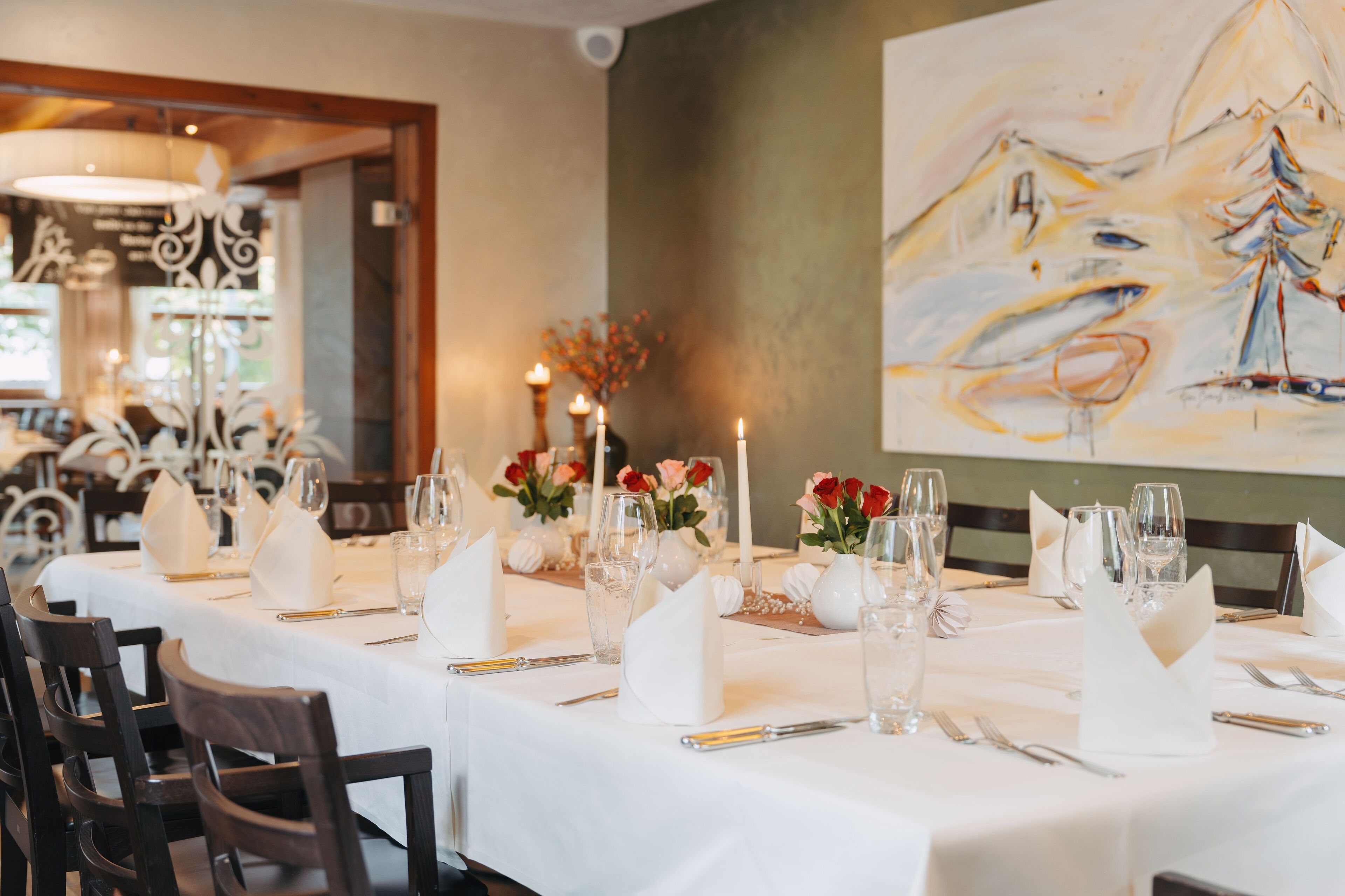 A restaurant with white tablecloths, neatly set tables, and candles.