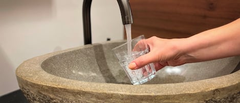 A hand holding a glass under a modern faucet in a stone sink.