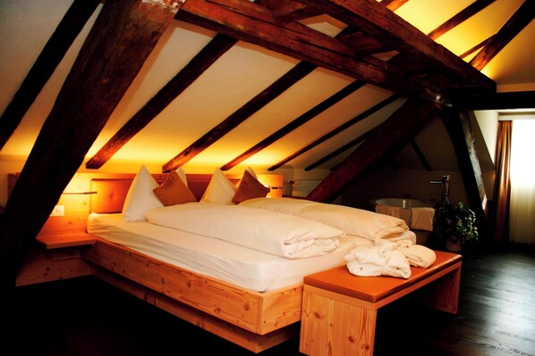 An attic bedroom with a wooden bed, pillows, a bedside table, and a bench.