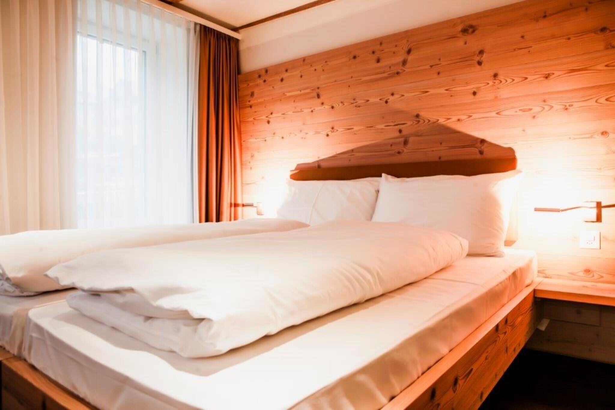 Cama doble con ropa blanca en una habitación con cabecera y mesitas de noche de madera.