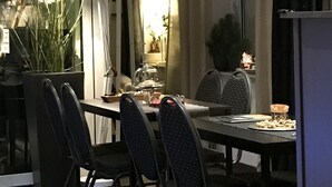 A dining area with a table set for four, surrounded by chairs. A large potted plant is to the left, and a lamp is on the table. The room has a modern design with a large window and curtains. - Apartment Hotel Lindeneck (Erfurt)