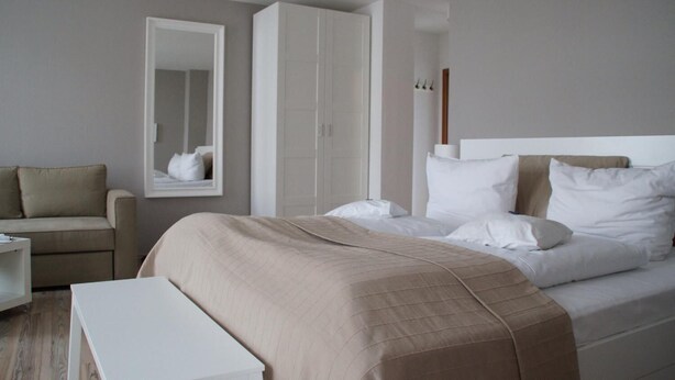 A modern hotel room with a bed, a chair, a wardrobe, and a mirror. - Apartment Hotel Lindeneck (Erfurt)